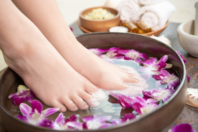 Pieds dans une bassine remplie d'eau et de fleurs violette